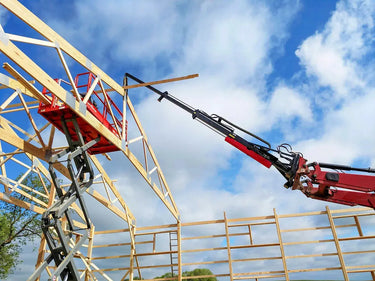 A crane is lifting a Telescoping Boom up to the roof of a building. The Telescoping Boom is long and heavy, and it looks like it will be used to support the roof.